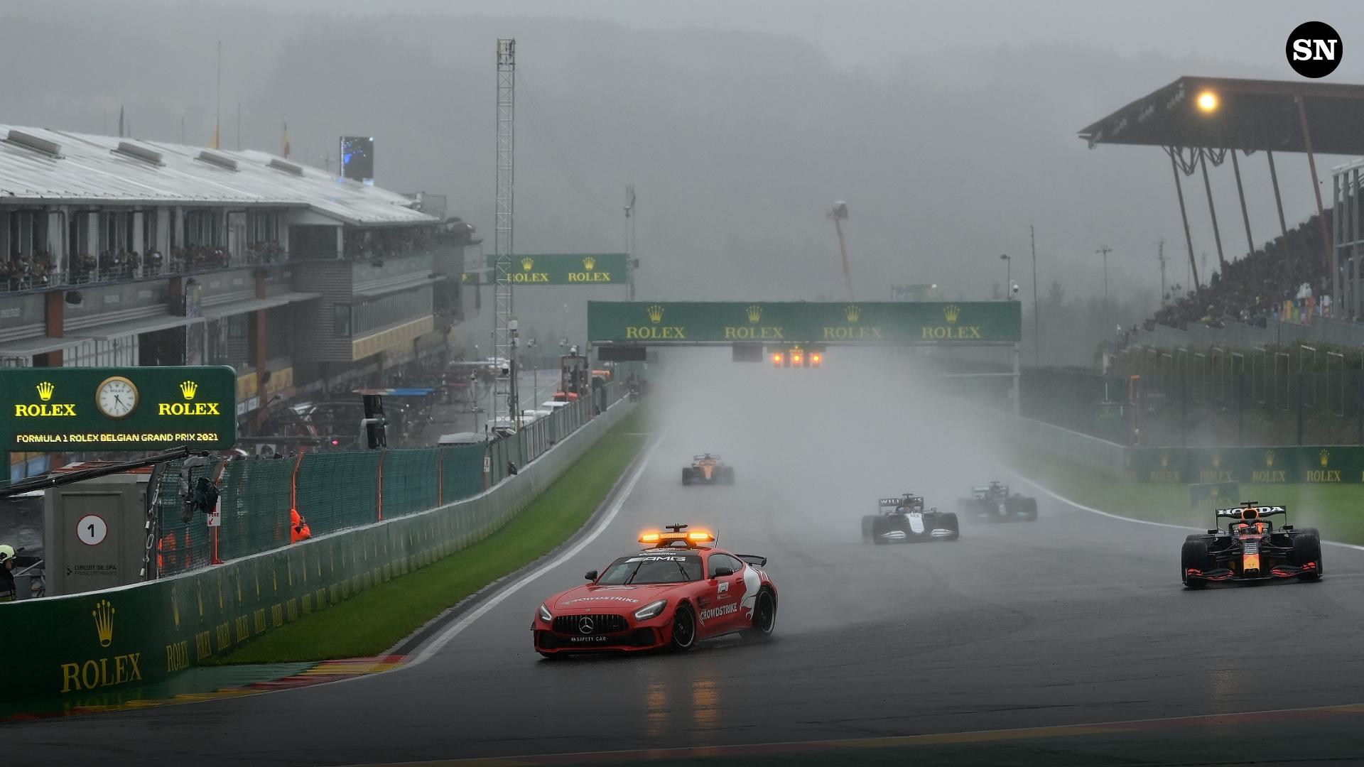 Vista amplia del Safety Car liderando el pelotón frente a las gradas de Spa-Francorchamps bajo intensa lluvia, con los semáforos de salida en rojo, GP de Bélgica 2021