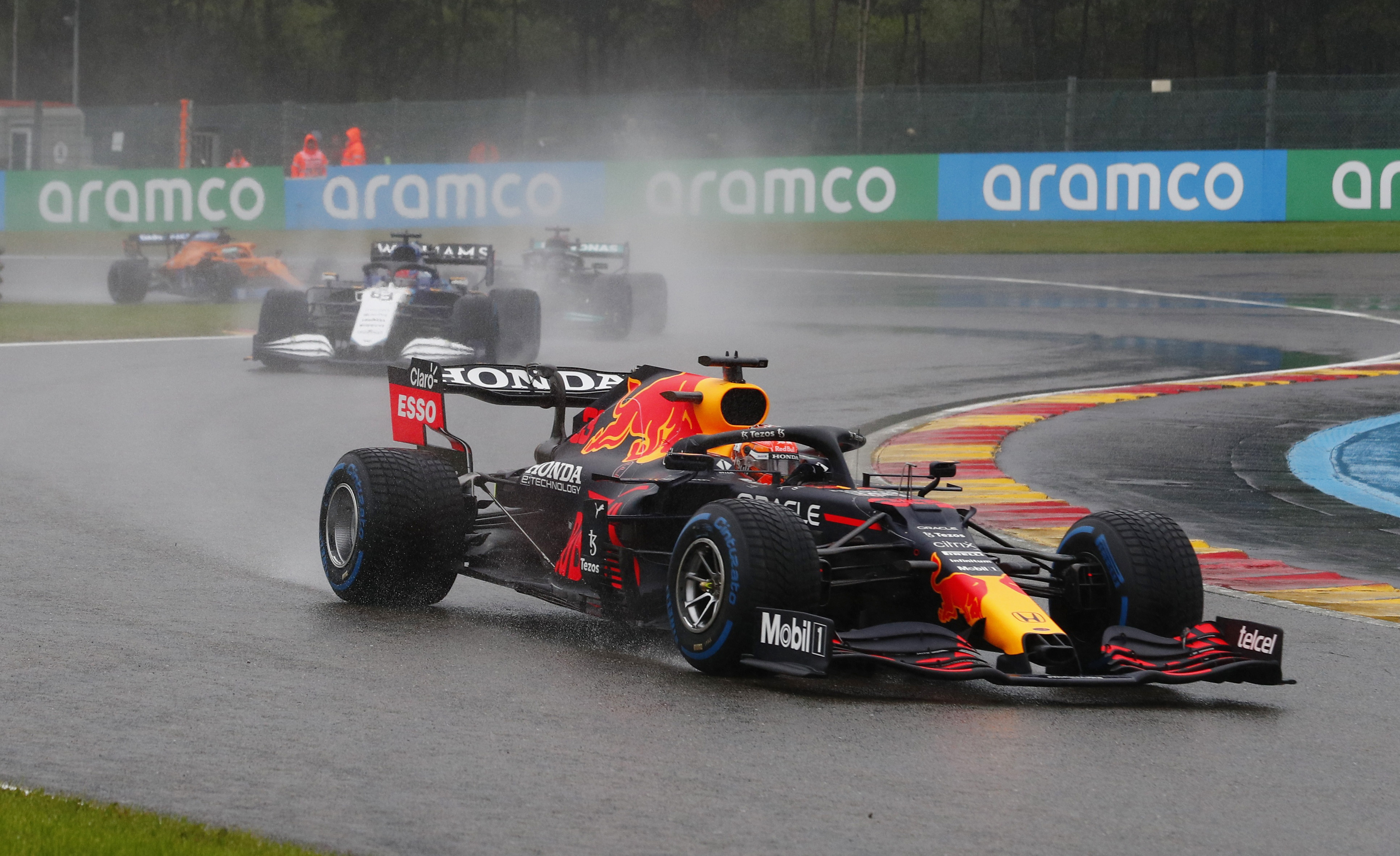 Primer plano del Red Bull de Max Verstappen tomando una curva bajo lluvia en Spa-Francorchamps, seguido de cerca por el resto del pelotón, GP de Bélgica 2021